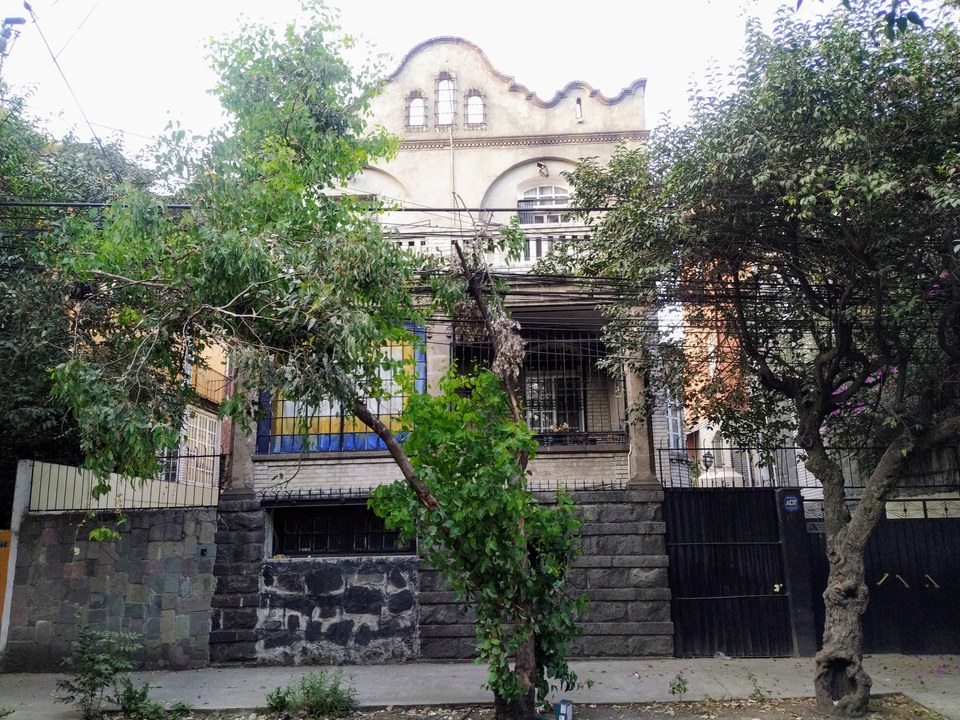A vintage two-story building with arched windows partially obscured by trees and electrical wires.