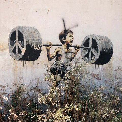 A mural depicts a young boy straining to lift a heavy barbell with peace symbols as weights.