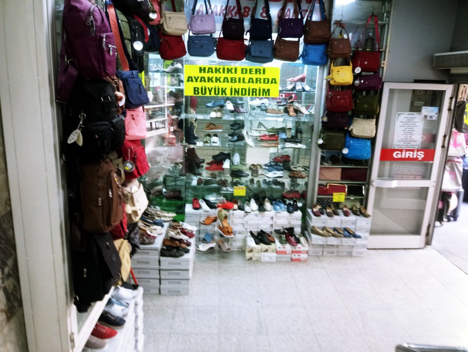 A shop display featuring various shoes and hanging handbags with a sale sign.