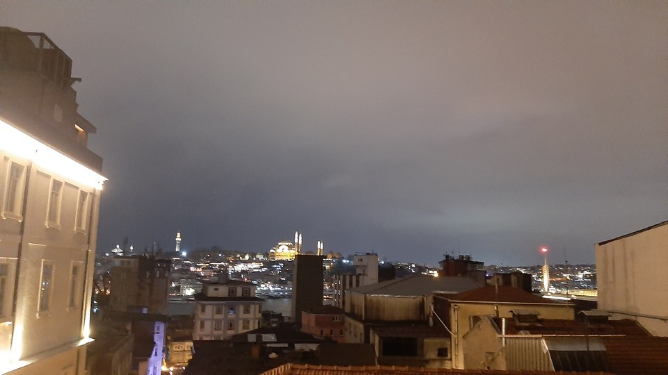 Nighttime cityscape with illuminated buildings and a cloudy sky.